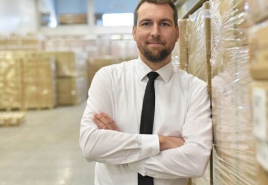 Warehouse manager leaning on boxes while he thinks about his ideal WMS and order processing platform